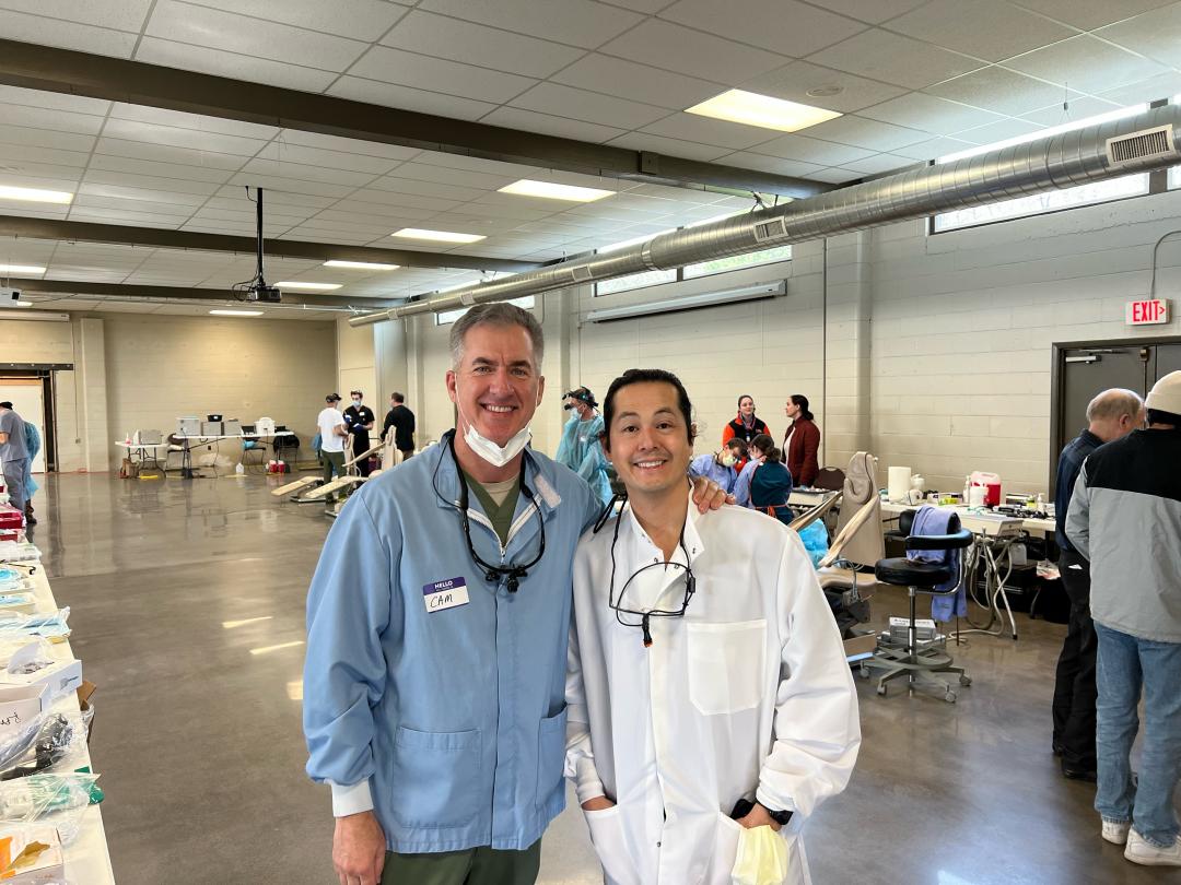 Two men in dentist gear pose for a picture.