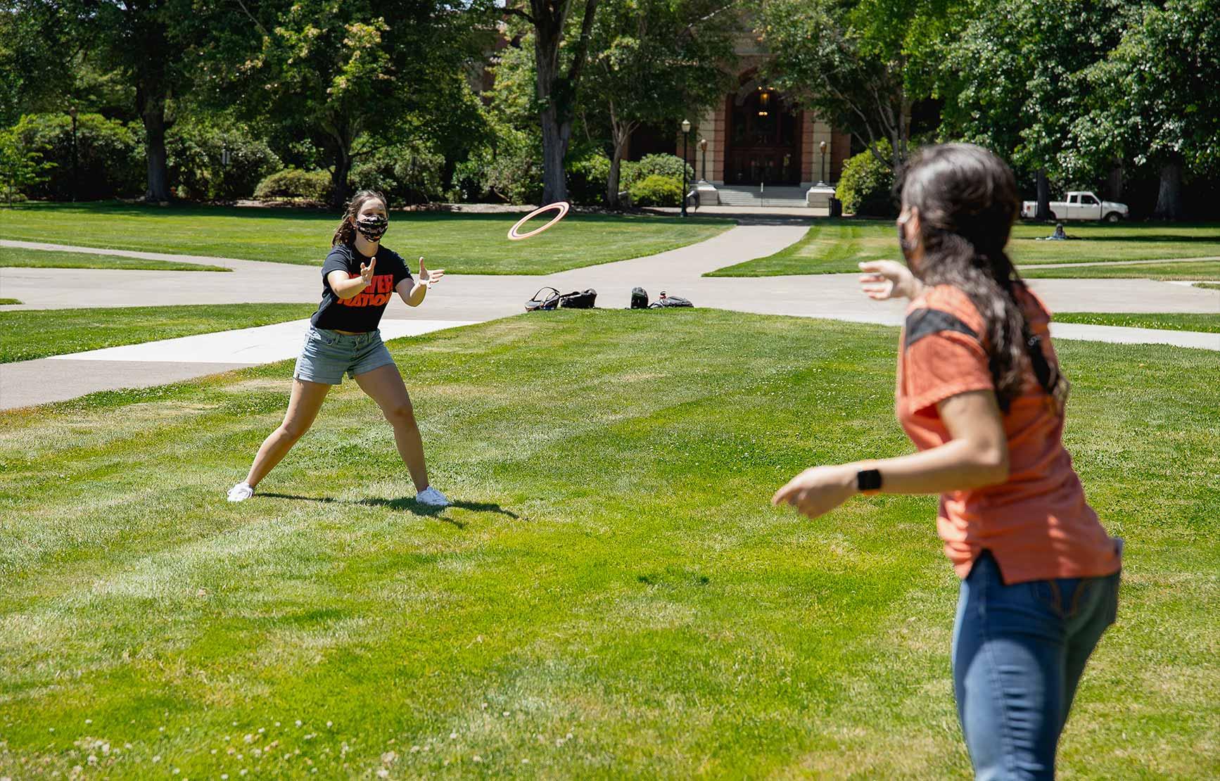 Students playing with frisbee outside the Memorial Union Quad while wearing masks.