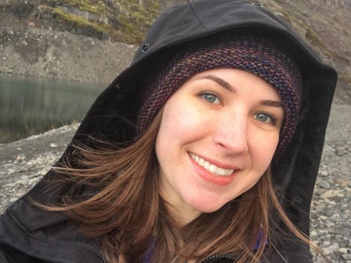 Hannah Kehlet-Delgado taking a selfie in a raincoat on a rocky sea shore.